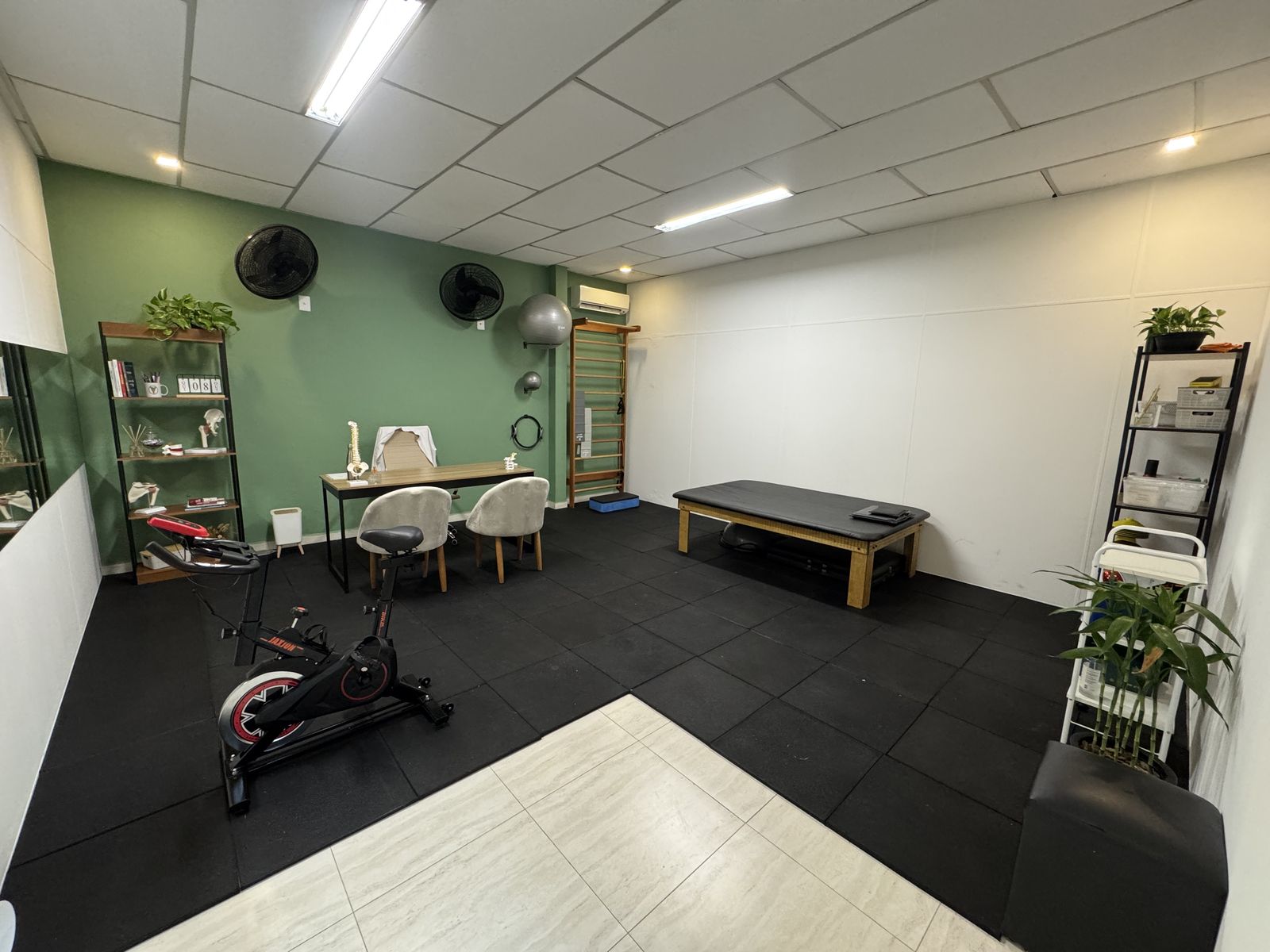 Sala de atendimento do consultório de fisioterapia em Peruíbe, com maca, espaldar, bicicleta ergométrica e mesa de avaliação