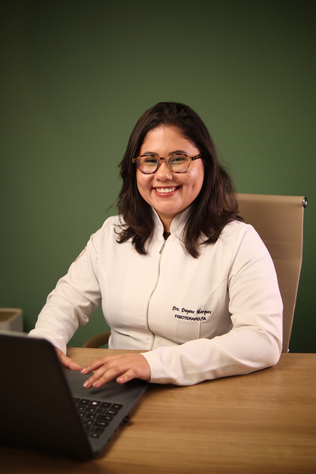 Dayane Marques, fisioterapeuta, sorrindo em sua mesa de atendimento no consultório em Peruíbe/SP